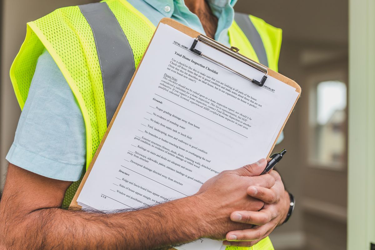 An inspector in a safety vest holds a clipboard with a home inspection checklist